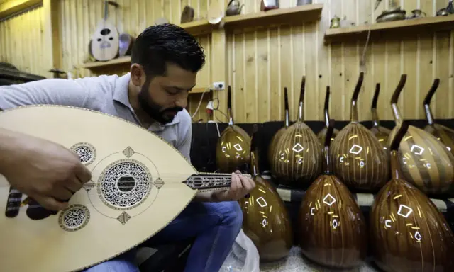Un joueur de oud expérimenté accorde son instrument, entouré d'autres ouds prêts à être joués.