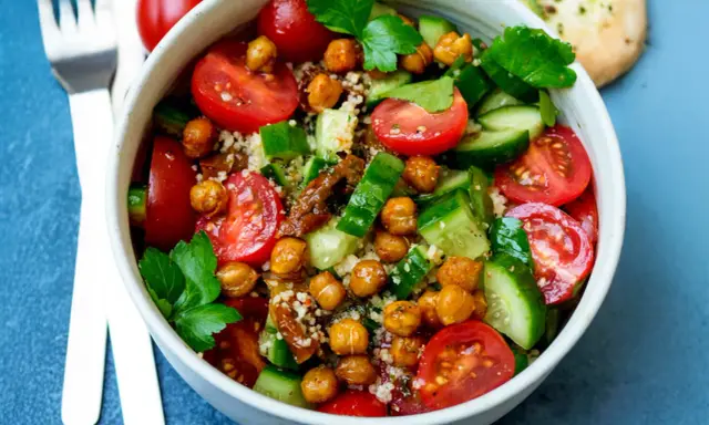 Frischer Couscous-Salat mit Kichererbsen, Tomaten und Gurken, garniert mit Petersilie.