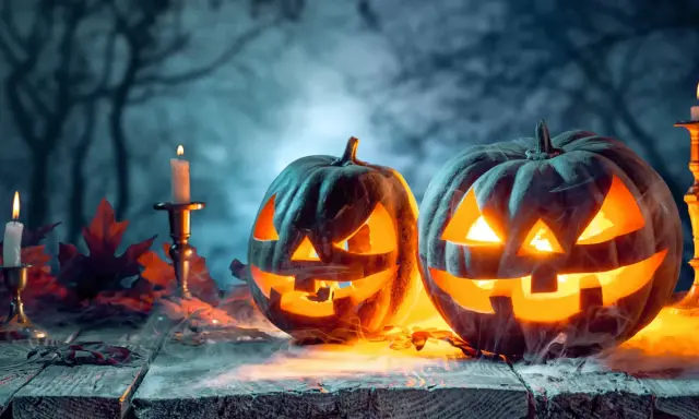 Zwei gruselige Kürbisse leuchten im Nebel, umgeben von Kerzen und Herbstlaub. Die wahre Bedeutung von Halloween liegt in dieser unheimlichen Atmosphäre.