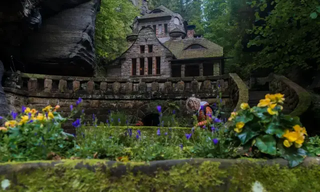 Kamienny domek w sercu czeskiej Szwajcarii, otoczony zielenią i kwitnącymi kwiatami.