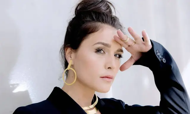 Jessie Ware, w czarnej marynarce, z dłonią na czole, jakby prosiła "say you love me". Złote kolczyki i naszyjnik dodają blasku.