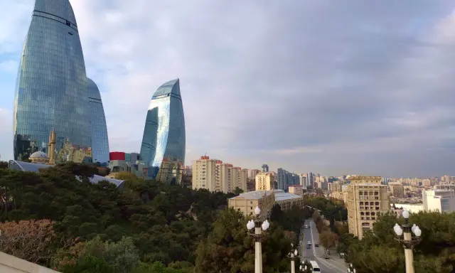 Płomienne wieże Flame Towers w Baku, które warto zobaczyć, górują nad miastem. W tle widać panoramę miasta i zielone drzewa.