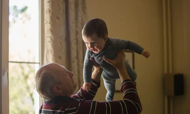 Dziadek podrzuca radosnego wnuka. Czy dziadkowie muszą płacić alimenty za syna? To pytanie, które nie ma związku z tą ciepłą chwilą.
