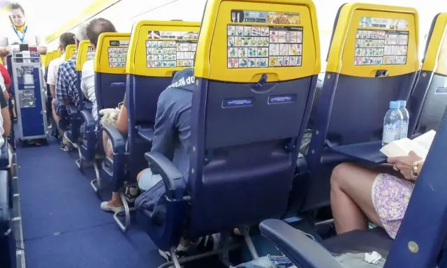 Wnętrze samolotu Boeing 737, rzędy miejsc dla pasażerów. Widok na siedzenia z żółtymi oparciami i instrukcjami bezpieczeństwa.