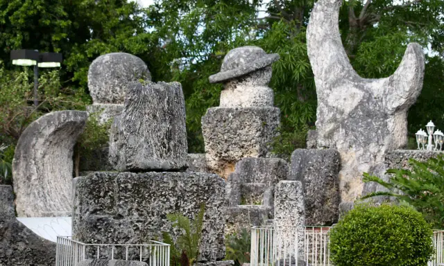Sculture in pietra calcarea e corallo, tra cui un cappello e una forma a mezzaluna, creano un magico coral castle immerso nel verde.