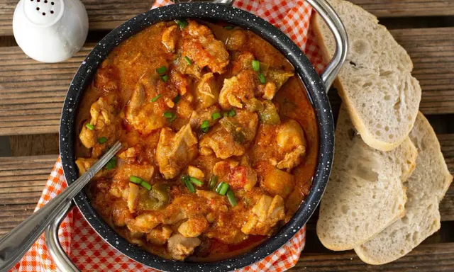 Pyszny gulasz z indyka w sosie pomidorowym, posypany szczypiorkiem, podany z chlebem.