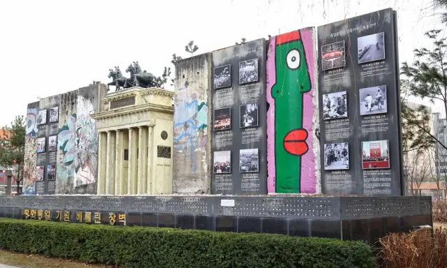 Fragment muru berlińskiego z graffiti i zdjęciami, obok replika Bramy Brandenburskiej.