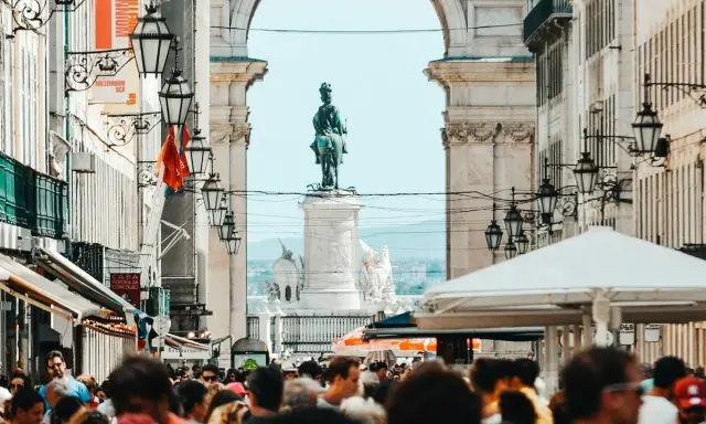 Menschenmenge auf der Rua Augusta in Lissabon mit Reiterstatue und Triumphbogen im Hintergrund.