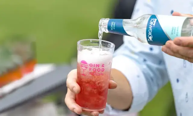 Tonic water wird in ein Glas mit rotem Getränk gegossen. Perfekt, um den Sommerdrink zu mischen.