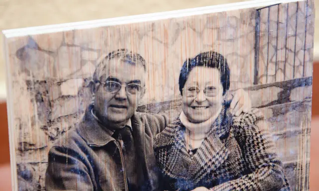 Pareja sonriente en un retrato transferir foto a madera, con un fondo de ladrillos y textura de madera visible.