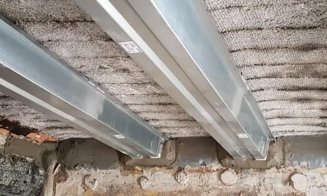 Vigas metálicas instaladas para como reforzar una viga de madera dañada por el fuego. Se observa el soporte de las nuevas vigas sobre la estructura existente.