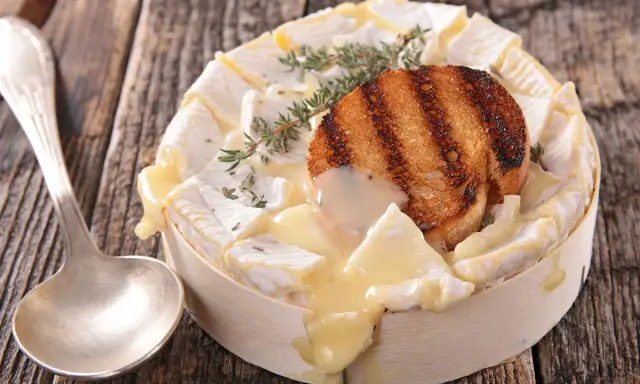 Un camembert coulant, plat typique normandie, garni d'une tranche de pain grillé et de thym, prêt à être dégusté avec une cuillère.