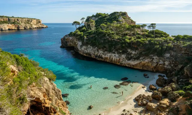 Malownicza zatoczka z turkusową wodą i piaszczystą plażą, otoczona klifami i zielenią. Idealne miejsce na relaks, jedna z pięknych palma de mallorca atrakcje.