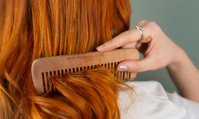 Mujer peina su cabello pelirrojo con un peine de madera. ¿En qué época del año se cae más el pelo? El otoño es conocido por ser el momento en que el cabello se cae más.