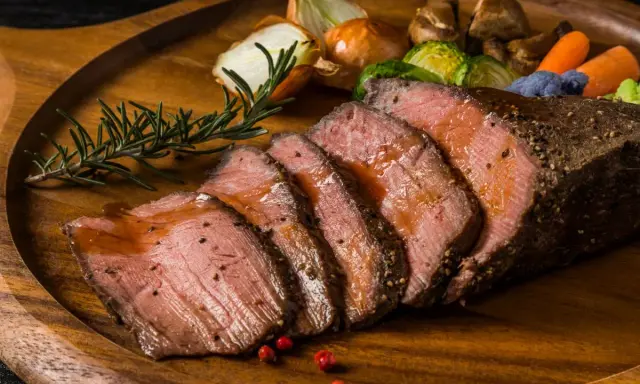Succulento arrosto di manzo affettato, servito su un tagliere di legno con verdure arrosto, cipolle e rosmarino.
