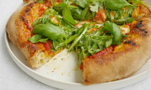 En närbild av en pizza med ruccola och basilika. Perfekt för ett enkelt pizzasås recept.