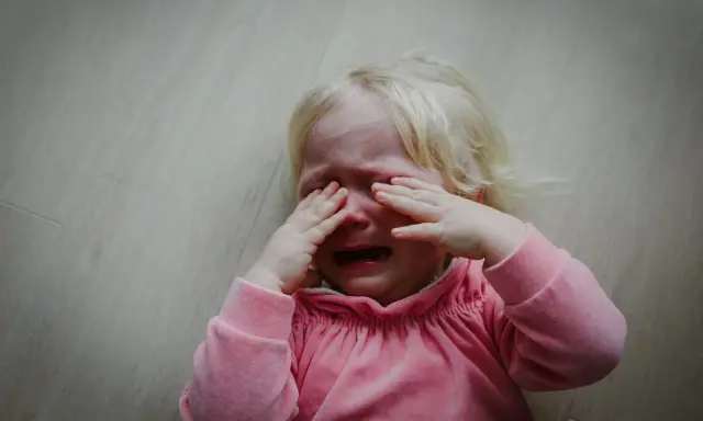 Małe dziecko uderza głową, płacząc. Może to być sygnał, że potrzebuje pomocy psycholog.