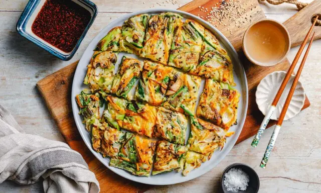 Bunte koreanische Pfannkuchen mit Gemüse, Pilzen und Karotten, serviert mit Dip und Stäbchen.