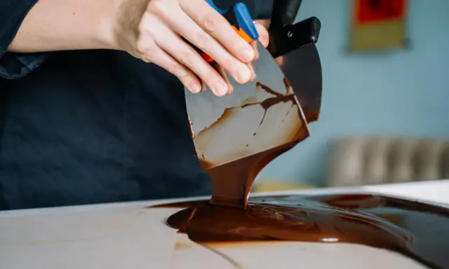 Mains travaillant du chocolat brillant sans tempérage avec des spatules. La texture fondante et lustrée promet une gourmandise parfaite.