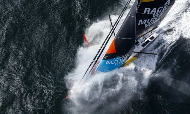 Le voilier de Boris Herrmann fend les vagues, projetant une gerbe d'eau. La voile arbore "Race we must win".