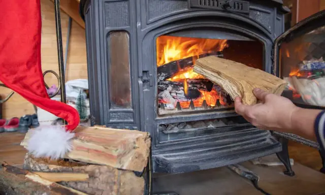 Une main ajoute du bois dans un poêle à bois allumé. Un bon choix de poêle à bois est essentiel pour un hiver chaleureux.