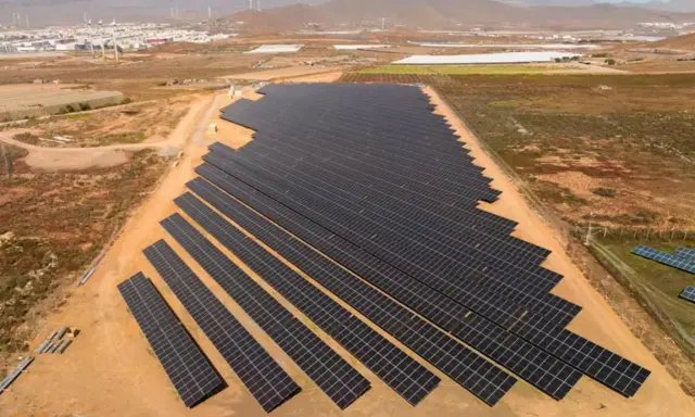 Große Solaranlage in Spanien, die die "Sonnensteuer" umgeht und saubere Energie liefert. Im Hintergrund Windräder und eine Stadt.