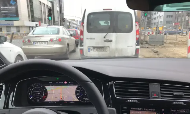 Utrudnienia na drodze, korek przed budową. Samochody stoją w deszczu, nawigacja pokazuje objazd.
