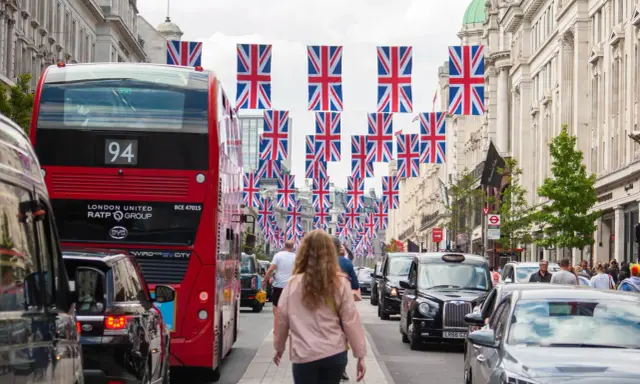 Ulica w Londynie ozdobiona flagami Wielkiej Brytanii. Widać czerwony autobus, czarne taksówki i ludzi. Święta w Wielkiej Brytanii w pełni!