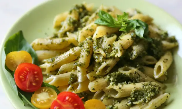 Penne z pesto i pomidorkami koktajlowymi. Pyszny obiad bez mięsa, udekorowany listkami bazylii.