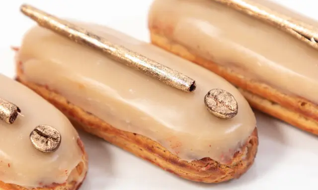 Trois éclairs gourmands, glacés à la crème pâtissière café, ornés d'une touche dorée et d'un grain de café scintillant.