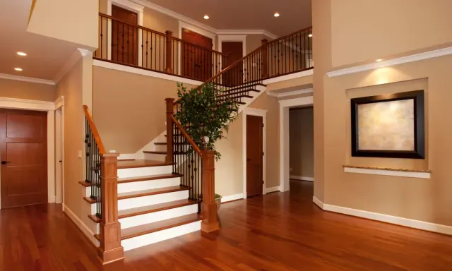Interno di una casa due piani moderna: scala in legno e metallo, porte in legno, un quadro e un albero decorativo.