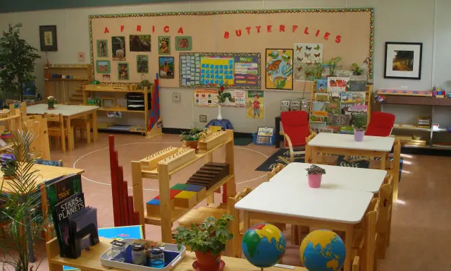 Klasa przygotowana zgodnie z metodą Montessori: globusy, książki o Afryce i motylach, materiały edukacyjne na półkach.