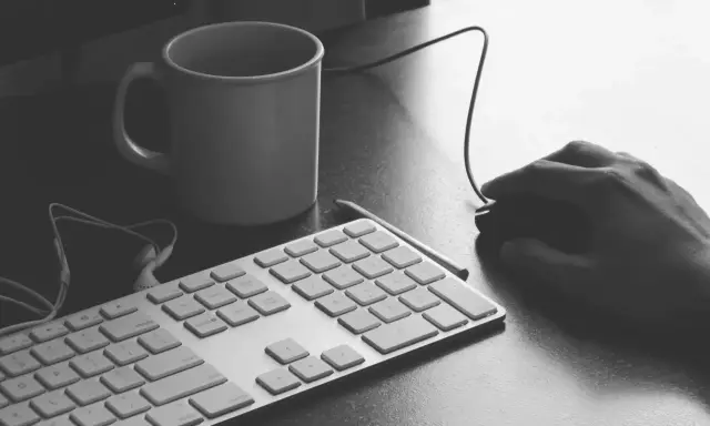 Ręka programisty nad klawiaturą, kubek kawy i myszka. Czas na programowanie aplikacji.