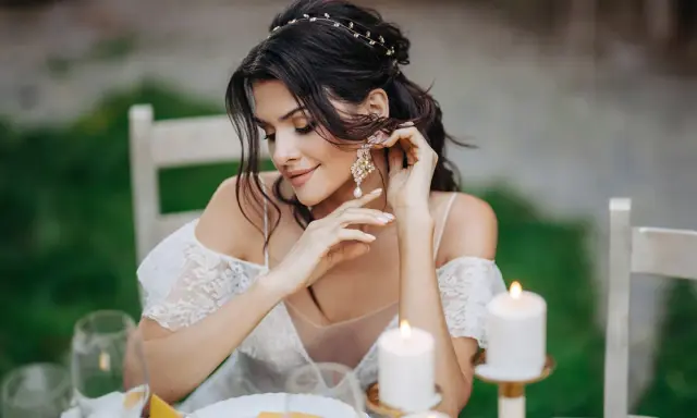 Piękna panna młoda poprawia swoje eleganckie kolczyki ślubne z perłami, przygotowując się do ceremonii.