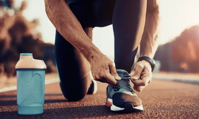 Uomo si allaccia le scarpe da corsa, pronto per correre a stomaco vuoto. Accanto, una borraccia blu.