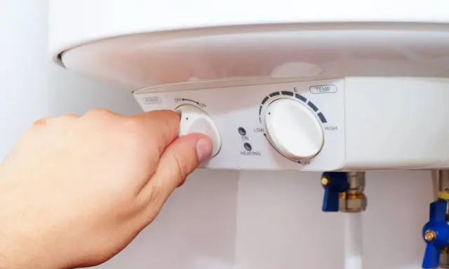 Mano ajustando el dial de potencia de un termo eléctrico. Si el termo pita, puede ser por un ajuste incorrecto de temperatura o por un problema de calentamiento.
