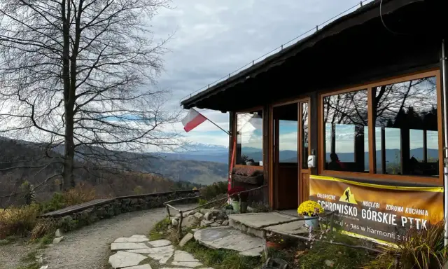 Bacówka pod Wierchomlą, schronisko górskie PTTK z widokiem na góry. Polska flaga powiewa nad wejściem.