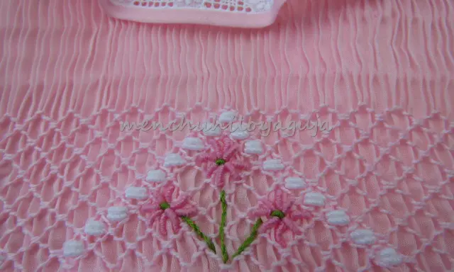 Detalle de puntada smock en tela rosa, con flores bordadas. Aprende como hacer punto smock.