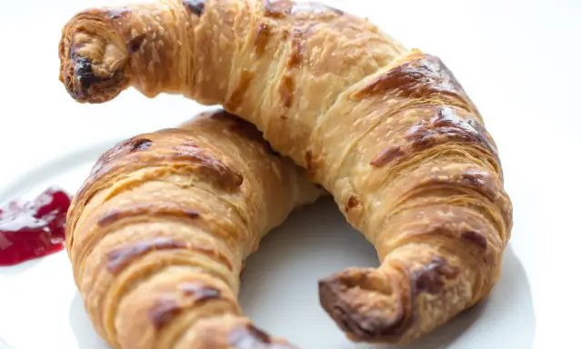 Två gyllene croissants med vaniljfyllning ligger på en vit tallrik. En klick hallonsylt bredvid.