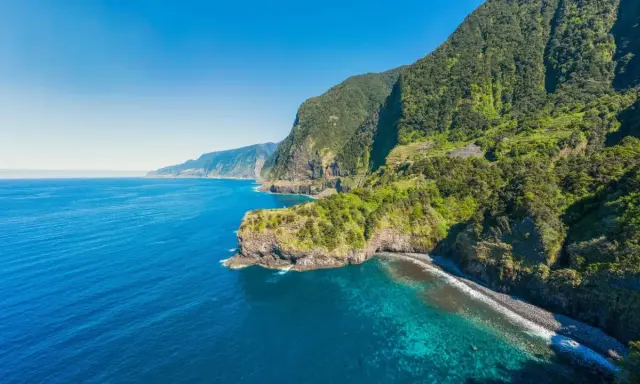 Grüne Berghänge stürzen ins türkisfarbene Meer. Ein perfekter Tag für eine Reise nach Madeira im Oktober.