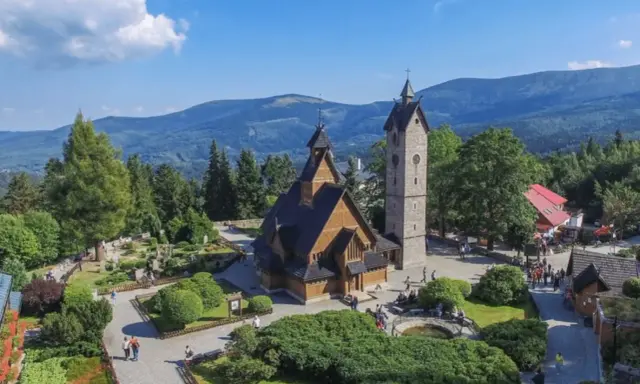 Drewniany kościółek i wieża na tle gór. Czy to Karpacz, czy Szklarska Poręba?