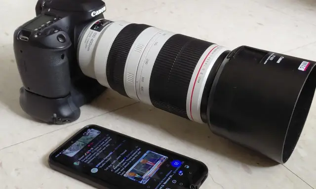 Canon 80D con obiettivo 100-400mm, pronto per una recensione. Sullo smartphone, un tweet su politica.
