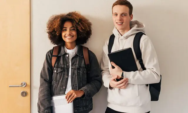 Dwóch studentów, dziewczyna z burzą włosów i chłopak z rudymi włosami, trzymają laptopy i zeszyty. To przykładowy artykuł po angielsku.