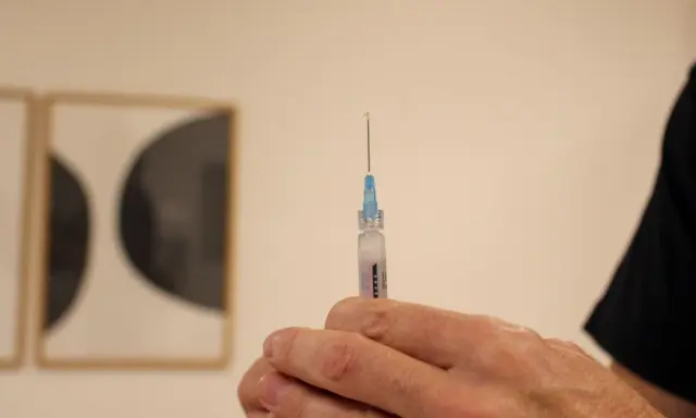 En hand håller en spruta med en droppe vaccin redo för injektion. Kanske en del av vaccin Singapore-programmet.