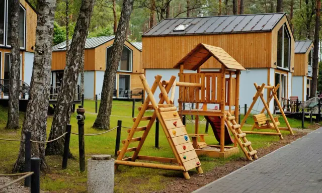 Drewniany plac zabaw z domkami w tle – idealne bory tucholskie atrakcje dla dzieci.