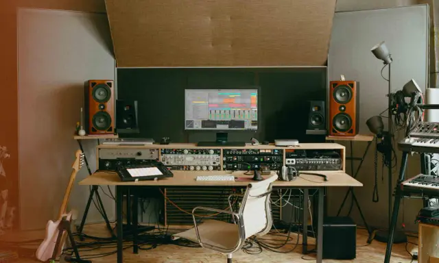 Un studio d'enregistrement avec des enceintes, un ordinateur affichant une station de travail audio numérique, des claviers, une guitare et divers équipements. C'est ici que le producteur de musique crée des sons.