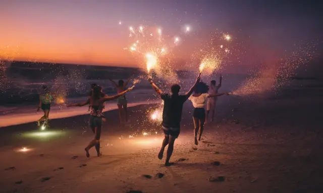 Giovani festeggiano il Ferragosto sulla Riviera Romagnola con scintille sulla spiaggia al tramonto.