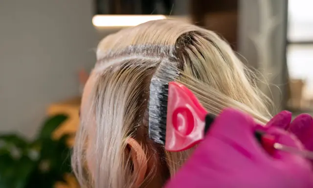 Profesjonalna dekoloryzacja włosów w salonie. Różowa rękawiczka i pędzel nanoszą produkt na blond pasma.