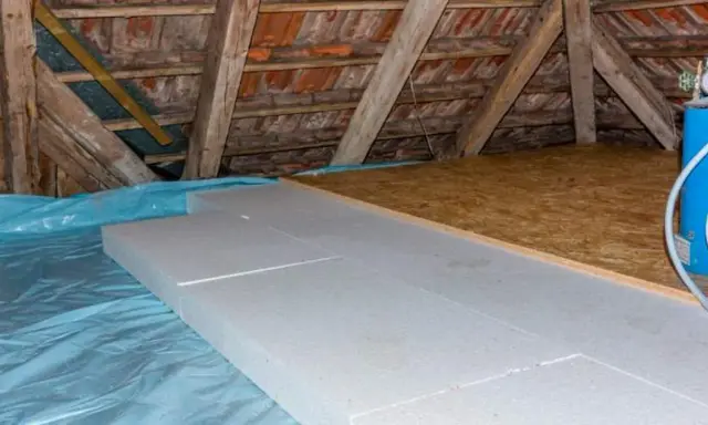 Aislamiento de suelo en una casa antigua con paneles de poliestireno sobre plástico azul, bajo vigas de madera y tejas.