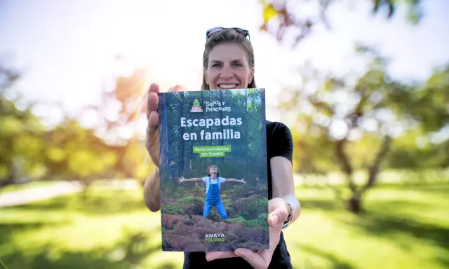Mujer sonriente muestra libro "Escapadas en familia", con un niño en portada, ideal para viajes inolvidables para niños por España.